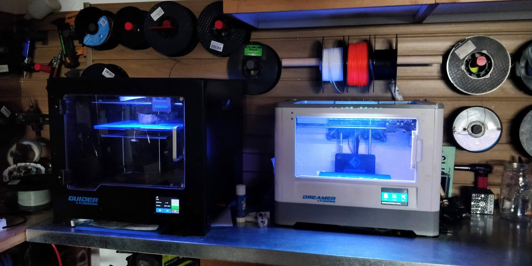 Two Flashforge printers running in front of a wall of filament spools